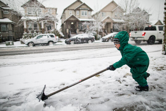 strong young boy shovels, pushes snow off the sidewalk