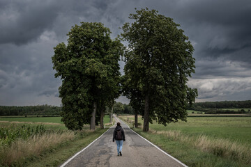a lone female walks down a road in rural countryside farming area of Belgium Ardennes. Woman has...