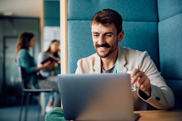 Happy entrepreneur surfing the net on laptop in office.