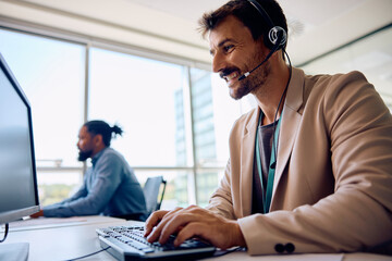 Happy male entrepreneur with headset working on computer in office.