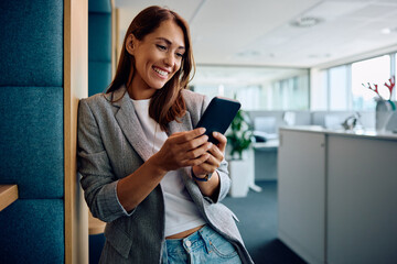 Happy female entrepreneur using smart phone in office.