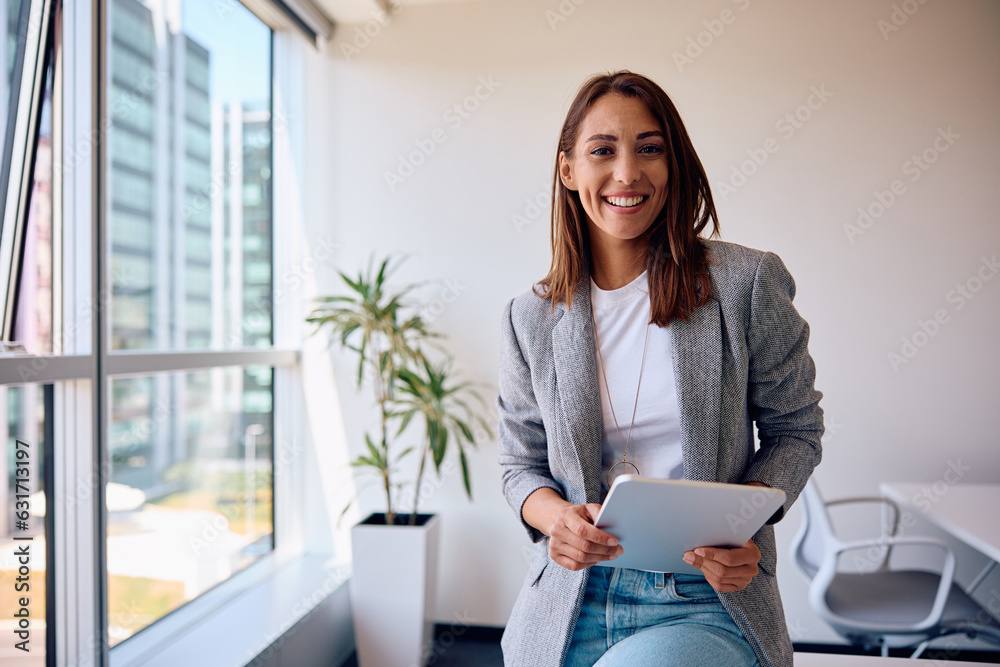 Wall mural Young happy businesswoman using touchpad while working in office and looking at camera.