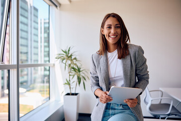 Young happy businesswoman using touchpad while working in office and looking at camera. - Powered by Adobe