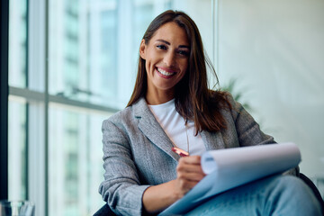 Happy female entrepreneur working on business reports in office and looking at camera.