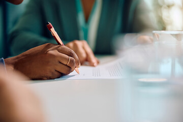 Close up of black woman signing agreement on meeting with insurance agent.