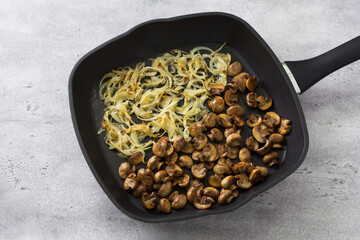 Frying pan with fried onions and mushrooms on a gray textured background. Step of preparing a homemade vegan dish