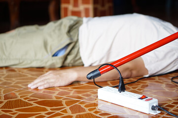 Using red plastic stick is moving away the electric plug socket from the unconscious man who lay...