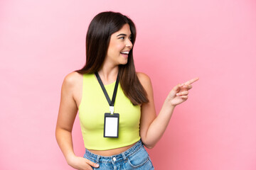 Young Brazilian woman with ID card isolated on pink background pointing finger to the side and...