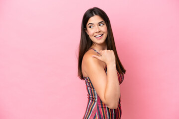Young Brazilian woman isolated on pink background pointing to the side to present a product