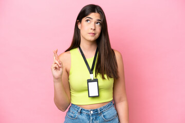 Young Brazilian woman with ID card isolated on pink background with fingers crossing and wishing the best