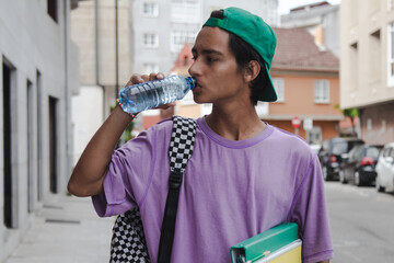 young man with backpack and books drinking water in the street