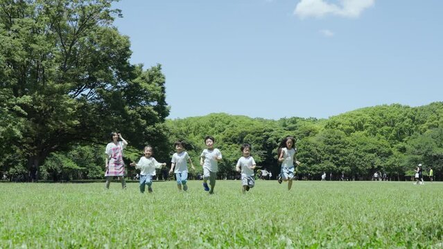 緑地でかけっこをする子供たちと、見守る女性