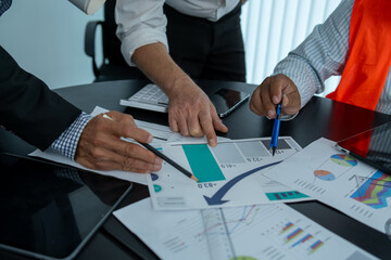 Business man and woman working together weekly analysis on laptop on tablet and blueprint in office.