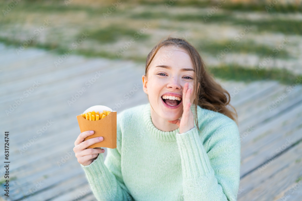 Poster Young pretty girl holding fried chips at outdoors shouting with mouth wide open