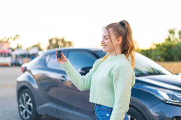 Young pretty girl holding car keys at outdoors with happy expression