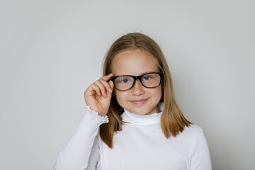 Happy smiling kid girl in glasses posing on white wall background, studio portrait