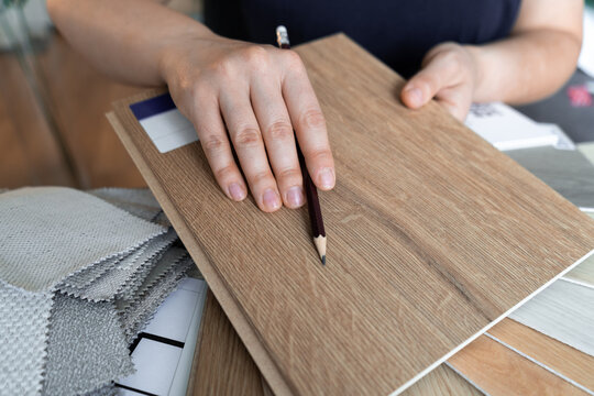 Female Interior Designer Showing Wooden Flooring Samples To Clients In A Design Studio. Woman Showcasing An Assortment Of Materials To Her Customers. Choosing Different Wood Floor Shades And Textures.