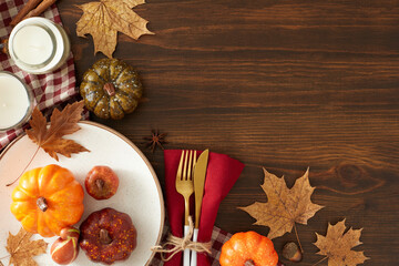 Gorgeous fall table arrangement. Top view of plate, cutlery, napkin, tablecloth, raw pumpkins, candles, anise, autumn leaves on brown wooden table background with empty space for advert or text