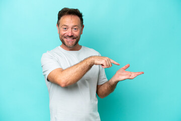 Middle age caucasian man isolated on blue background holding copyspace imaginary on the palm to insert an ad