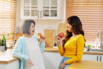 Obraz na płótnie Canvas Happy asian woman daughter hugging senior mother in the kitchen room eating healthy food happy enjoying.