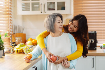Happy asian woman daughter hugging senior mother in the kitchen room eating healthy food happy enjoying.
