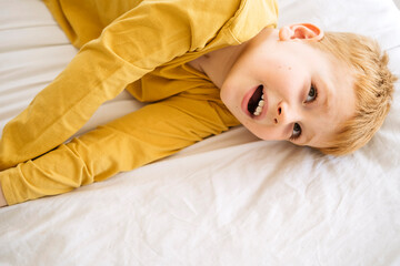 Obraz premium A playful red-haired boy finds comfort and joy on a pure white bed, a portrait of youthful energy
