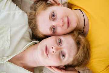 Two red-haired sisters lie cheek to cheek and look at the camera. Similar women with fair skin and freckles. 