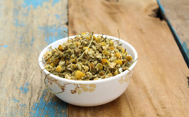Dried chamomile flowers in a bowl on wooden background 