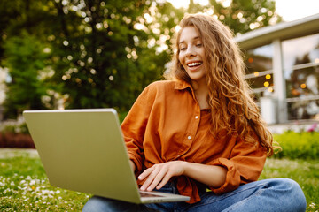 Portrait of a young beautiful female freelancer sitting on a green meadow with a laptop. Education...