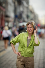 A woman enjoys music on headphones while standing on a street.