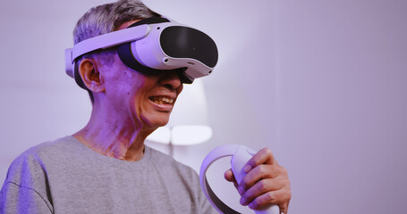 Asian old man having fun playing games while wearing virtual reality glasses at home.