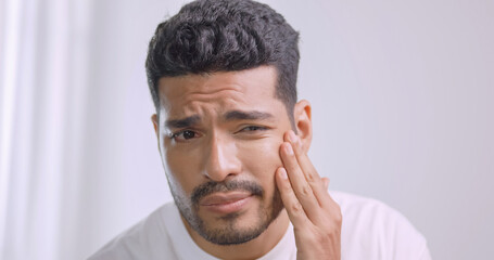 A young man worried about the wrinkles on his face while standing in front of mirror in bathroom at home.