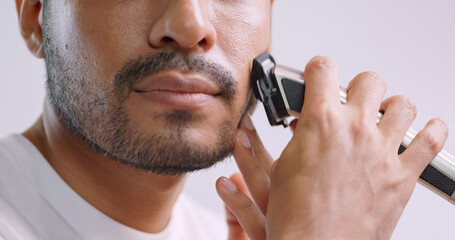 A man is using electric shaver to trim mustache and beard while standing in front of mirror in...