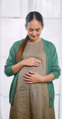 Happy Asian pregnant woman lovingly touching her unborn child while standing by the window of the house.