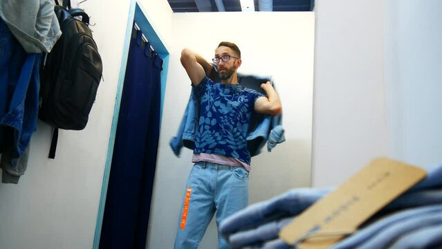 The reflection of a man in a fitting room trying on a denim jacket and pants