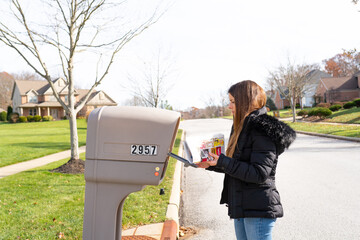 YOUNG WOMAN LOOKING FOR POSTAL MAIL AT HER MAILBOX.