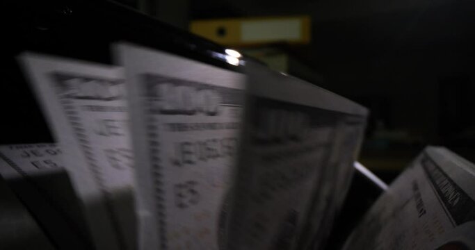 Bill counter processing dollar bills in dark premise. Counting money in bank. Modern technology and accountants take turns slow motion