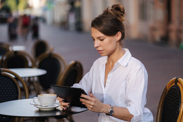 Portrait of attractive female freelancer using tablet in cafe on terrace
