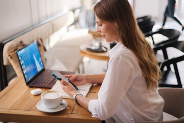 Side view of female student using laptop in cafe. Lady in formal white shirt smile.