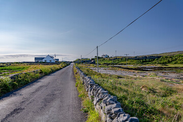 Fototapeta na wymiar Asphalt road with stone walls and power line alongside on a bright sunny day with a blue sky on Inishmore island, Galway