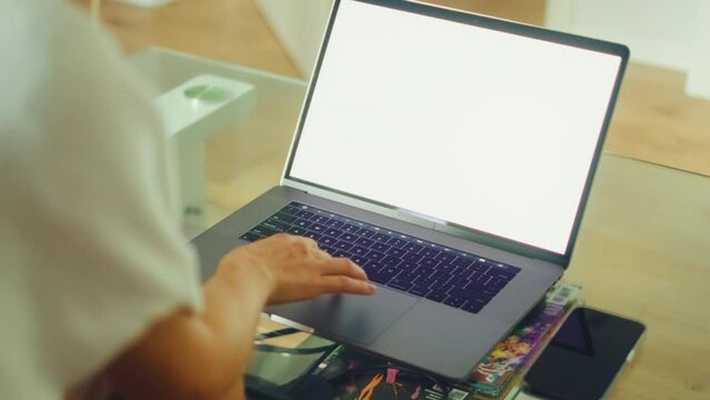 Young caucasian woman sitting on sofa at home and using laptop computer with white blank screen, mock-up.
