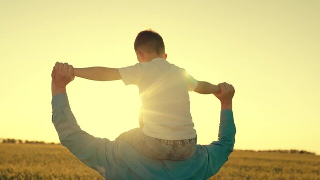 father carries child shoulders. happy father walking with little son wheat field. farmer shows his child fields wheat sunset field. summer harvest. Child dreams becoming airplane pilot. shoulder