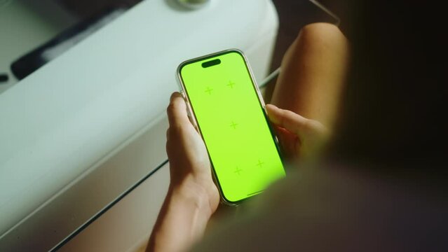 Young woman sitting on sofa at home and uses Mobile phone with green screen Mock-up. 