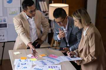 Group of confident business people point to graphs and charts to analyze market data, balance sheet, account, net profit to plan new sales strategies to increase production capacity.	