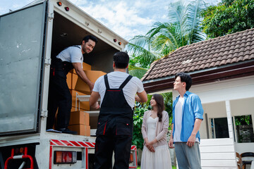 Asian Couple check while unloading boxes and furniture from a pickup truck to a new house with service cargo two men movers worker in uniform lifting boxes. concept of Home moving and delivery. - obrazy, fototapety, plakaty