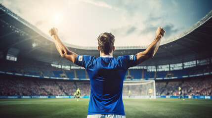 Back view of football player in blue t-shirt with arms raised at stadium