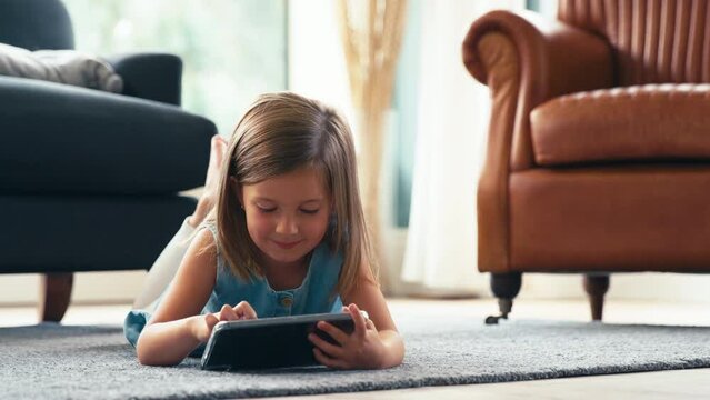 Young girl lying on floor of lounge at home playing game or streaming movie to digital tablet - shot in slow motion