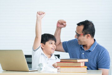 Cheerful indian family, child son with father have fun raising fist hands up together while doing...
