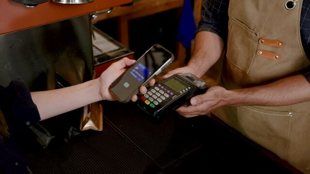 Barista standing at counter in cafe, submit payment scanner for want transfer money without cash, customer handed in phone scan pay for drink, check mark appeared, meaning payment was completed.
