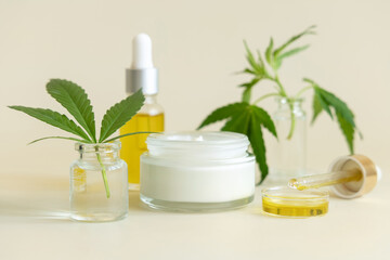Obraz na płótnie Canvas Cream Jars and bottles near green cannabis leaves close up on light yellow. CBD cosmetics